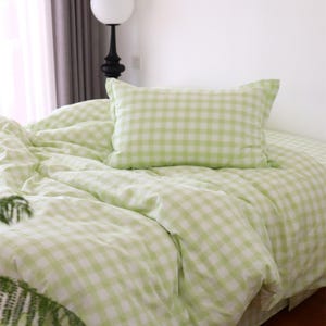 May include: A bed covered with a light green and white gingham patterned duvet and pillow. The bedding is soft and wrinkled, suggesting a comfortable and inviting atmosphere. The color scheme is fresh and bright.