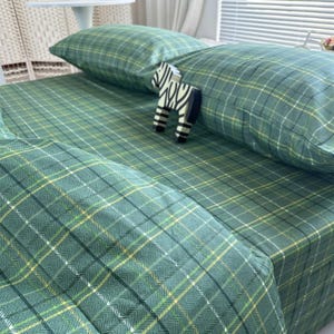 Op de afbeelding: Groen geruit beddengoed met een kussen en een hoeslaken. Het patroon bevat gele en witte lijnen. Een klein zebrafiguur staat op het bed.