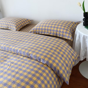 Puede incluir: Un juego de cama con un patrón de cuadros vichy en amarillo y azul. El conjunto incluye una funda nórdica y dos fundas de almohada rectangulares a juego. La tela muestra un diseño de cuadrícula consistente en todas las piezas.