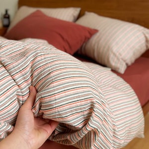 Puede incluir: Una cama con cabecero de madera y un juego de ropa de cama. La ropa de cama incluye un edredón a rayas con rayas rojas, blancas y verdes, y almohadas y sábanas rojas lisas. Las almohadas tienen un estampado de rayas.