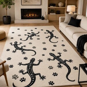 May include: A rectangular area rug featuring a cream-coloured background with a repeating pattern of black lizards and small black and grey paw prints scattered across the surface. The lizards have detailed geometric markings along their bodies.