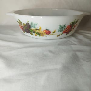 May include: White oval serving bowl with a colorful vegetable design. The bowl features a pattern of tomatoes, corn, squash, and other produce. The bowl has two handles.