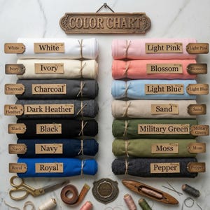 Puede incluir: Una carta de colores muestra muestras de tela enrolladas en varios colores, incluyendo blanco, marfil, carb&oacute;n, gris oscuro, negro, azul marino y real. Otros colores son rosa claro, flor, azul claro, arena, verde militar, musgo y pimienta. Cada rollo est&aacute; etiquetado.