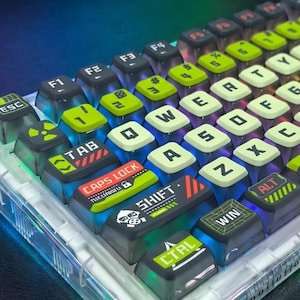 May include: A mechanical keyboard with a clear plastic case and colorful keycaps. The keycaps are a mix of black, green, and white, with various symbols and text. The keyboard has a futuristic, tech-inspired design, with the text "LIGHT POLLUTION" visible.