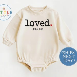 May include: Cream-colored baby romper with long sleeves. The word "loved" is printed in black, with a small red heart. Below the word is "John 3:16". A blue circle with white text that says "SHIPS NEXT DAY" is on the bottom right.