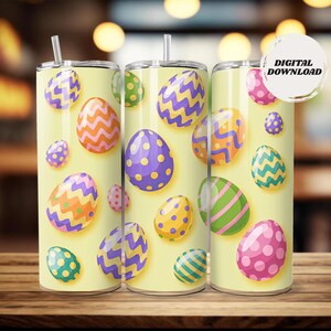 Può includere: Tre bicchieri gialli a tema pasquale con colorati disegni di uova. Le uova presentano vari motivi, tra cui strisce, pois e zig-zag, nelle tonalità del viola, rosa, verde e arancione. Ogni bicchiere ha un coperchio argentato e una cannuccia.