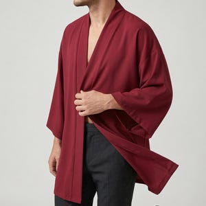 Może przedstawiać: Bordowy szlafrok w stylu kimono z szerokimi rękawami. Szlafrok jest otwarty z przodu i noszony z ciemnoszarymi spodniami. Tkanina wydaje się lekka i zwiewna, co sugeruje swobodny krój.