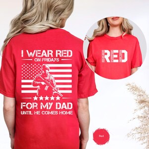 Könnte beinhalten: Rotes T-Shirt mit weißem Text und Grafiken. Auf der Rückseite des Shirts steht der Text "I WEAR RED ON FRIDAYS" über einem weißen amerikanischen Flaggen-Design mit einer Soldaten-Grafik. Darunter steht der Text "FOR MY DAD UNTIL HE COMES HOME".
