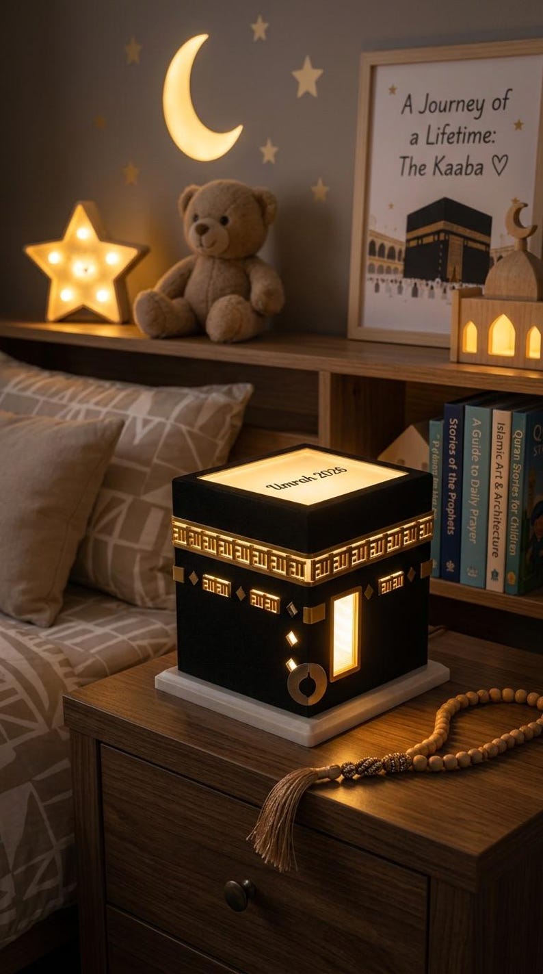 A close-up of the Kaaba night light on a wooden nightstand, featuring gold decorative trim, a glowing door, and the customized text Umrah 2026 on the illuminated top panel.