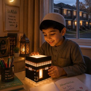 Child smiling while using a warm illuminated Kaaba night light in a cozy Muslim bedroom.