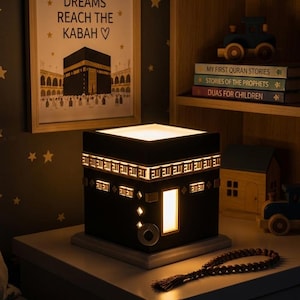 A black Kaaba night light glows on a nightstand in a dimly lit children room.
