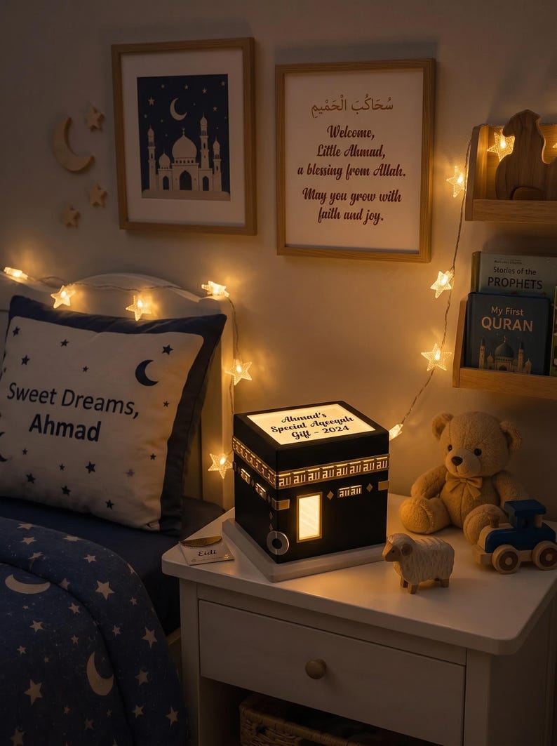 A child bedroom setting features a customized Kaaba night light on a white nightstand, next to books, a teddy bear, a wooden toy sheep, and a pillow reading Sweet Dreams Ahmad.