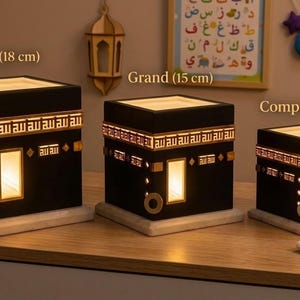 Three sizes of the black Kaaba night light are displayed on a shelf labeled Royal, Grand, and Compact.