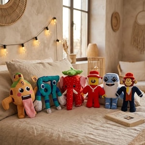 May include: A collection of colorful plush toys, including a number 9, a number 6, a strawberry elephant, a Lego-like figure, a blue and white creature, and a monkey. The toys are arranged on a bed with a neutral-toned comforter.