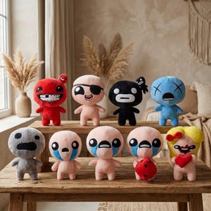 May include: A collection of plush dolls with various expressions and colors, including red, black, blue, and gray. Some dolls have eye patches, tears, or other unique features. They are arranged on a wooden surface.
