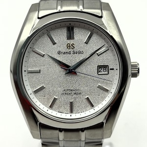 Könnte beinhalten: Eine silberfarbene Grand Seiko Automatik-Armbanduhr mit strukturiertem silberfarbenem Zifferblatt. Die Uhr verfügt über eine Datumsanzeige bei 3 Uhr und ein silberfarbenes Armband. Das Zifferblatt zeigt "Grand Seiko" und "Automatic Hi-Beat 36000".