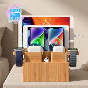 May include: A bamboo charging station with multiple slots for electronic devices. It features spaces for a tablet, two smartphones, two smartwatches, and wireless earbuds. The devices are charging, indicated by lightning bolt icons on the screens.