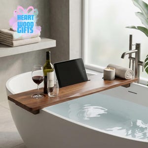 May include: A wooden bathtub tray with a wine glass, wine bottle, and a tablet. A lit candle and rolled towel are on the tray. The tray is over a white bathtub filled with water. The text "HEART WOOD GIFTS" is in the upper left corner.