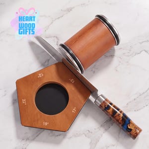 May include: A wooden knife sharpening guide with a pentagonal shape featuring angle markings of 12, 15, 17, 19, and 22 degrees. A metal knife with a patterned wood and blue resin handle rests across the guide, positioned near a cylindrical wooden object.