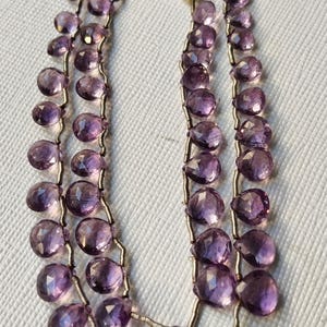 May include: Two strands of amethyst gemstone beads with silver wire and tassels. The beads are a deep purple colour and are teardrop-shaped. The tassels are made of silver-coloured threads.