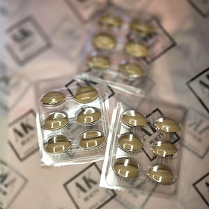 May include: Several sets of false eyelashes in clear plastic packaging. Each set contains six individual lashes with a reflective, gold-colored backing. The packaging is on a patterned surface with the text "AK BEAUTY".