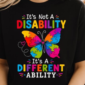 May include: A black short-sleeved t-shirt featuring a colorful butterfly graphic made of puzzle pieces. The text reads: It's Not A DISABILITY It's A DIFFERENT ABILITY. The design includes vibrant red, yellow, blue, green, and purple colors.