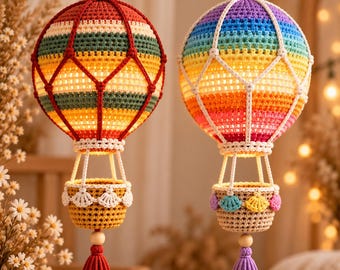 May include: Two hanging hot air balloon decorations made of crocheted yarn. The left balloon features horizontal stripes of red, green, and yellow with a white net overlay. The right balloon has rainbow stripes with a white net and a tassel.
