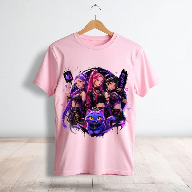 Pode incluir: Uma t-shirt de manga curta rosa claro com uma impress&atilde;o gr&aacute;fica de tr&ecirc;s personagens estilo anime e um gato roxo. O design inclui salpicos de tinta preta, pequenos cora&ccedil;&otilde;es, estrelas e caracteres de texto coreano no lado direito.