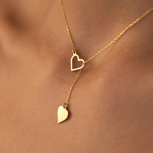 Può includere: Una delicata collana d'oro con due ciondoli a forma di cuore. Il cuore superiore è un contorno aperto, mentre il cuore inferiore è pieno. La collana pende da una sottile catena, creando un design semplice ma elegante. È un bel gioiello.