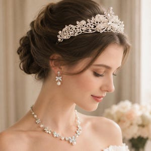 May include: A silver-toned tiara, drop earrings, and a necklace set featuring clear crystals and white pearls. The tiara has an intricate floral-inspired design, while the necklace and earrings feature matching crystal and pearl accents.