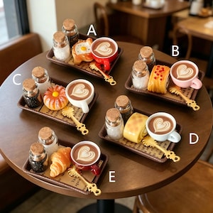 May include: Miniature coffee sets displayed on a round wooden table. Each set features a coffee cup with latte art, a pastry, a decorative spoon, and small glass jars with cork lids. The sets are presented on small brown trays.