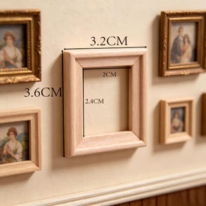 Pode incluir: Uma moldura retangular em miniatura de madeira clara sem acabamento. A moldura tem uma largura externa de 3,2 cm e uma altura de 3,6 cm, com uma abertura interna medindo 2 cm de largura e 2,4 cm de altura. É exibida entre outras molduras.