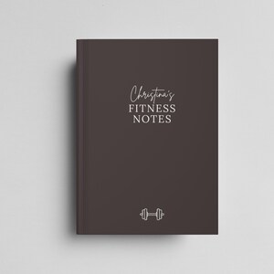 May include: A dark brown notebook with the text "Christina's FITNESS NOTES" in white script. A white dumbbell icon is at the bottom. The notebook is rectangular and has a clean, minimalist design.