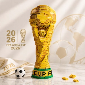 Puede incluir: Un trofeo amarillo construido con ladrillos, que se asemeja al trofeo de la Copa Mundial de la FIFA, con una base verde y la palabra "CUP" en negro. También se ve un balón de fútbol y el texto "2026 FIFA WORLD CUP".