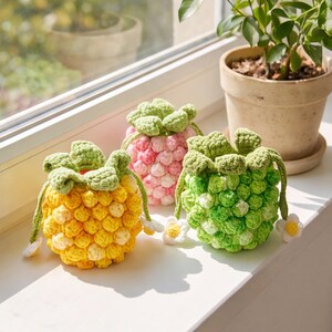 May include: Three small, round, crocheted drawstring pouches shaped like fruits. One is yellow, one is pink, and one is green, each featuring a textured bobble stitch pattern, green crocheted leaves at the top, and small white flower accents.