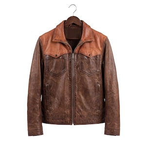 May include: A two-tone leather jacket featuring a dark brown body and a lighter tan yoke across the shoulders. The jacket includes a full-length front zipper, a classic collar, two chest pockets with buttoned flaps, and long sleeves with cuffs.