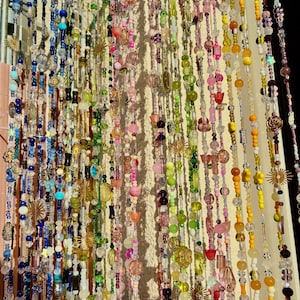 Pode incluir: Uma colorida cortina de contas com fios de vários comprimentos. As contas são num arco-íris de cores, incluindo azul, verde, rosa, amarelo e roxo. Alguns fios têm encantos decorativos como estrelas e flores. A cortina é provavelmente usada como um divisor de ambientes decorativo.