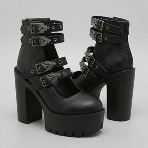 Può includere: Sandali neri con plateau e più cinturini con fibbie argentate ornate. I tacchi hanno un tacco a blocco spesso e una suola platform. Le scarpe hanno una cerniera sul retro del tallone.