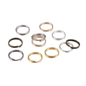 May include: A collection of split key rings in various metallic finishes, including silver, gold, and bronze. The key rings are arranged on a white surface, showcasing their different colors and designs. These rings are ideal for organizing keys or crafting.