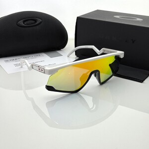 K&ouml;nnte beinhalten: Wei&szlig; gerahmte Sonnenbrille mit gelb-orange verspiegelten Gl&auml;sern. Die Sonnenbrille wird mit einem schwarzen Etui und einer schwarzen Schachtel mit dem Markennamen pr&auml;sentiert. Ein Reinigungstuch und Papiere sind ebenfalls sichtbar.