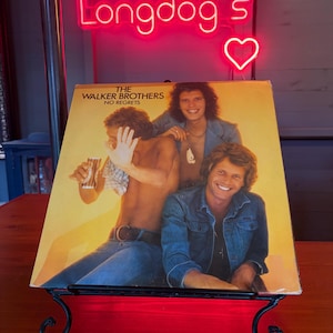 May include: A vintage vinyl record album cover for "The Walker Brothers" with the text "No Regrets." The cover features three men in denim jackets and shirts. A neon sign above reads "Longdog's" with a heart symbol.