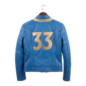 May include: A blue leather jacket featuring a gold-colored collar and the number 33 in large gold-colored numerals on the back. The jacket has long sleeves, a stand-up collar, and visible seam detailing across the shoulders and back panels.