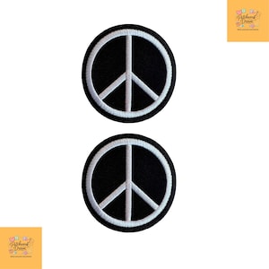 May include: Two circular embroidered patches featuring a white peace symbol centred on a solid black background. Each patch has a thick white stitched border, creating a clean contrast between the black fabric and the white thread design.