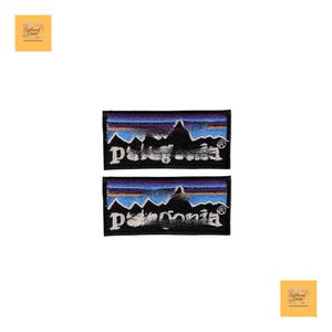 Op de afbeelding: Twee rechthoekige patches met het Patagonia-logo. De patches tonen een zwart silhouet van een bergketen, met een blauwe en gele lucht. Het woord "Patagonia" is in het wit geborduurd.