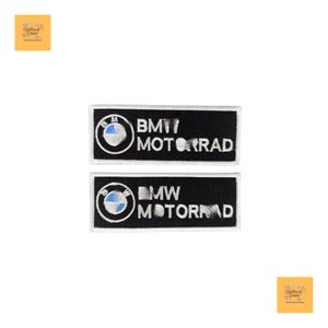 Op de afbeelding: Twee zwarte rechthoekige patches met witte randen. Elke patch heeft het BMW-logo en de tekst "MOTORRAD" in het wit. Het BMW-logo is een witte cirkel met blauwe en witte kwadranten en de letter "M".
