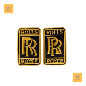 May include: Two rectangular patches featuring the Rolls Royce logo. The patches have a black background with gold lettering and a gold border. The logo includes the letters "RR" and the words "ROLLS ROYCE".