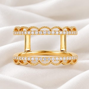 Pode incluir: Um anel duplo de ouro com duas bandas paralelas ligadas por barras verticais de ouro. Cada banda é adornada com uma fila de pequenas pedras transparentes de corte redondo e um rebordo delicado e recortado com contas em cima e em baixo.