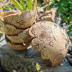 Op de afbeelding: Een stapel van drie beige keramische kommen en één losse kom, elk voorzien van ingewikkelde, handgedrukte botanische en geometrische patronen, waaronder bloemen, bladeren, spiralen en gearceerde texturen op hun afgeronde, getextureerde oppervlakken.