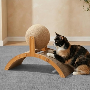 以下が含まれることがあります： サイザルボールと湾曲した段ボール製の引っかき面を備えた猫用スクラッチャー。木製のフレームがボールと引っかきパッドを支えています。三毛猫が引っかき面に寄り添っています。