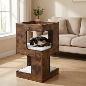 Op de afbeelding: Een houten kattenhuis met een donkerbruine afwerking. Het heeft een vierkant ontwerp met een slapende kat op een wit kussen binnenin. De kat is een mix van zwart, bruin en wit. Het huis heeft een lager platform.